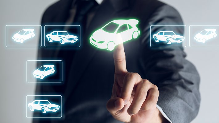 Im Vordergrund sind grafisch verschiedene Autotypen digital dargestellt, eine Männerhand wählt eines der Autos mit dem Zeigefinger per Klick darauf aus.