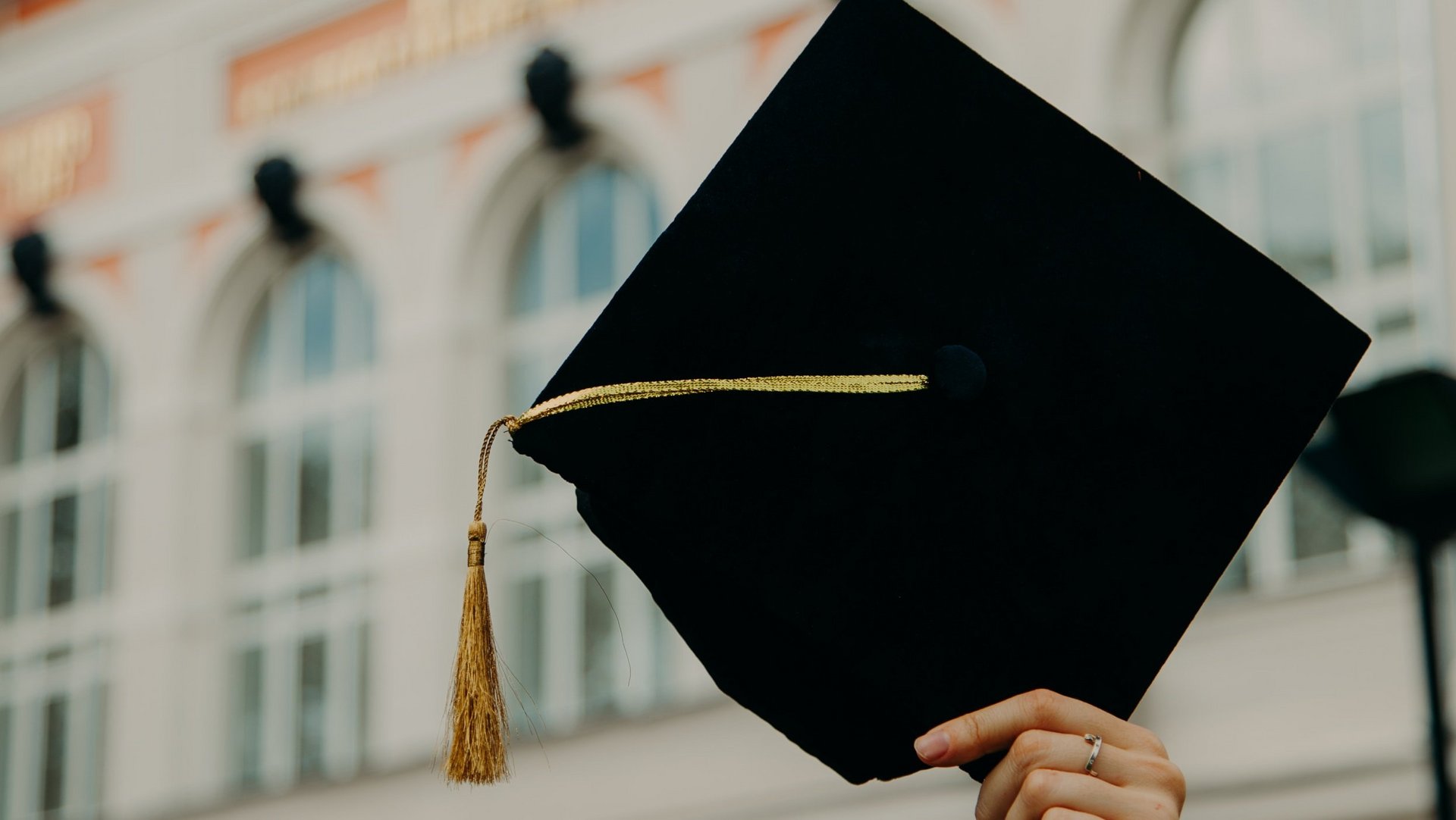 Traditionelle Kopfbedeckung für die Abschlussfeier bei Hochschulen wird von einer Frauenhand in die Luft gestreckt