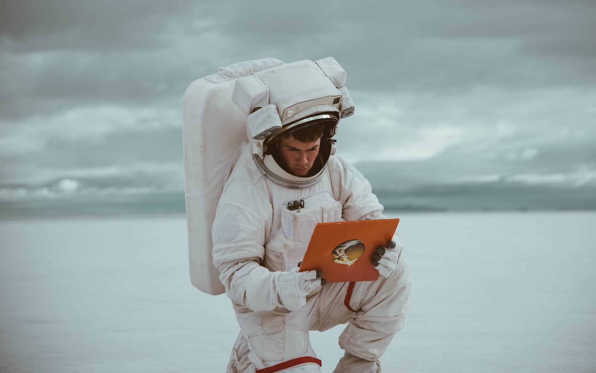 Astronaut kniet in einer kargen Landschaft, hält Tablet in den Händen und liest etwas darauf